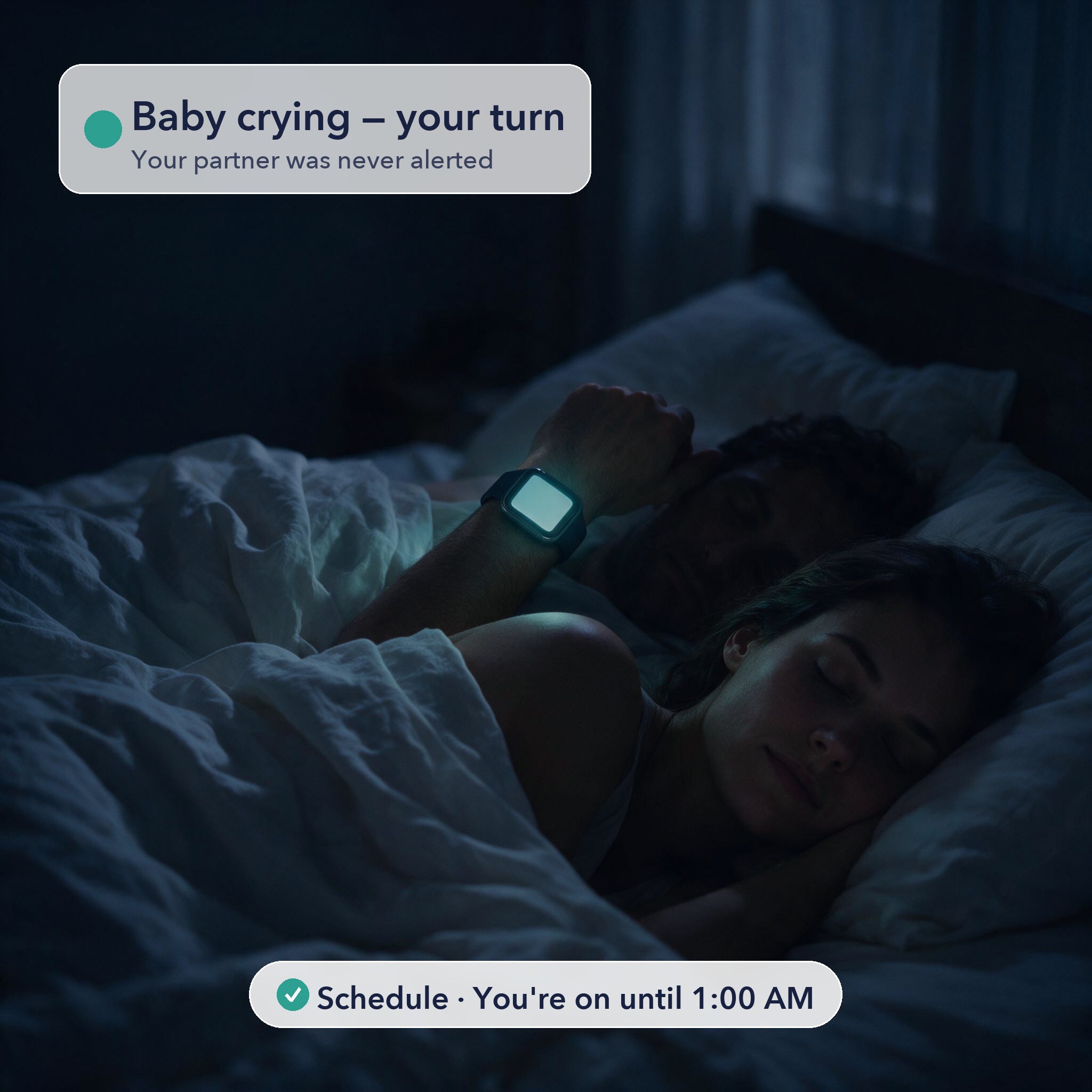 A couple asleep in a dark bedroom at night. Only one partner's smartwatch is lit, showing a Dozzi alert reading Baby crying, your turn. The other partner sleeps on, undisturbed.